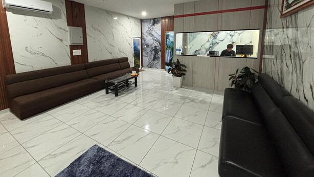 Un lobby moderno con una pared de mármol, una mesa de recepción, un sofá marrón y un sofá negro.