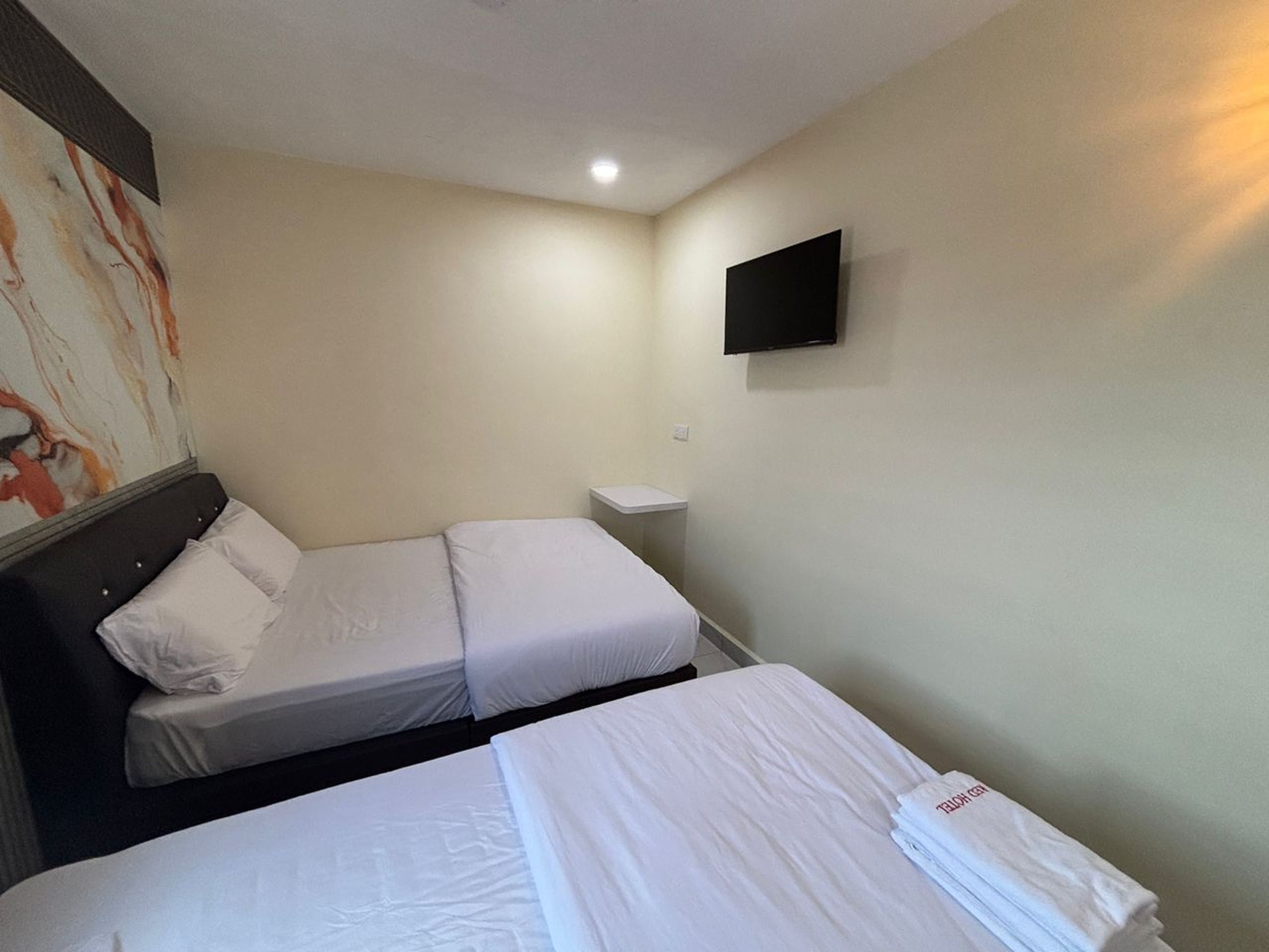 Quarto de hotel com duas camas de solteiro, uma televisão de tela plana na parede e um quadro na parede esquerda.