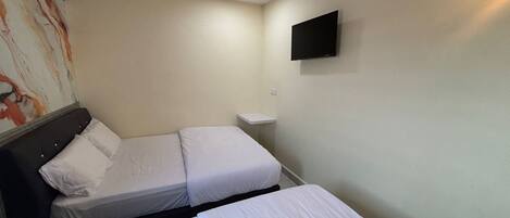 Quarto de hotel com duas camas de solteiro, uma televisão de tela plana na parede e um quadro na parede esquerda.