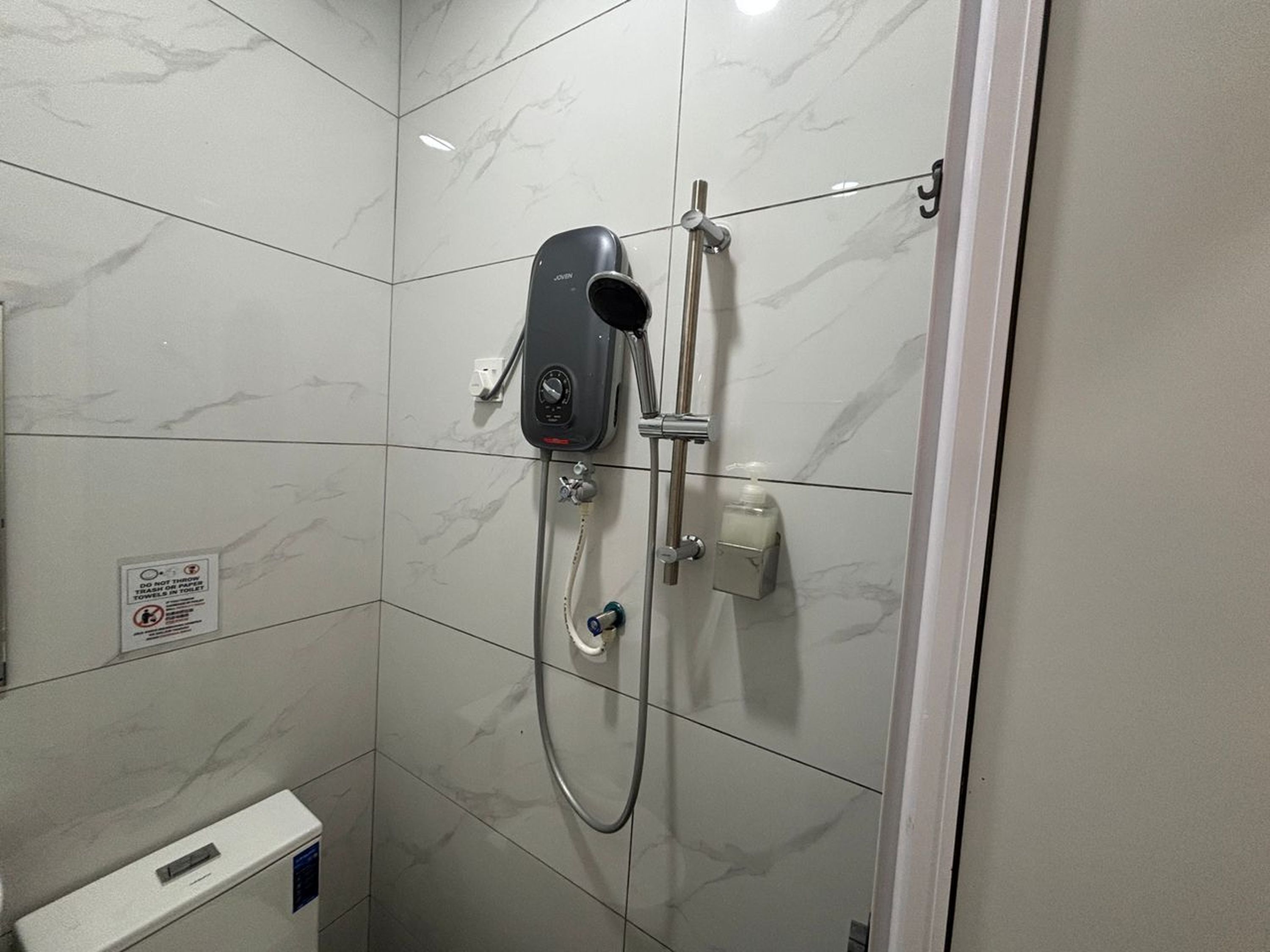 A bathroom with a shower, a soap dispenser, and a sign on the wall.