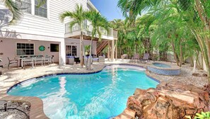 Ein Pool mit geschwungener Form, umgeben von Palmen und einer Terrasse mit Gartenmöbeln.
