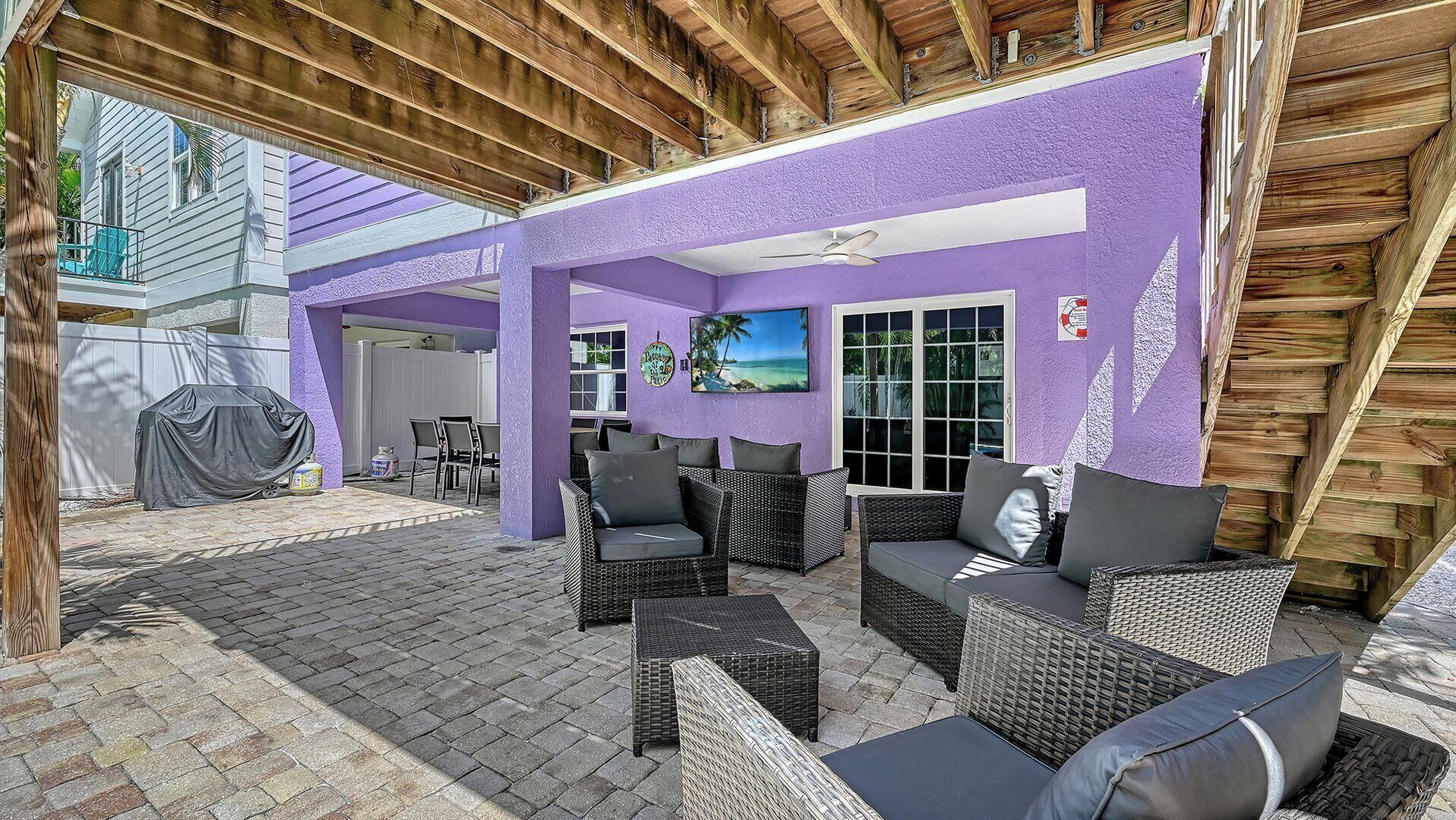 An outdoor patio area with wicker furniture, a covered barbecue, and a view of a neighboring house.