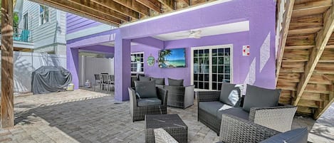 An outdoor patio area with wicker furniture, a covered barbecue, and a view of a neighboring house.
