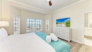 Ein Hotelzimmer mit Bett, Kommode, Fernseher und Blick auf den Strand.