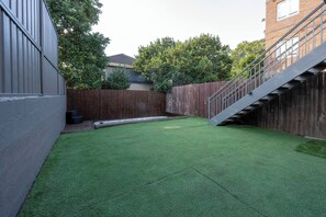 A backyard with artificial grass, a wooden fence, and a staircase leading to a building. - Garden Apartment in Centre of Bondi (Sydney)