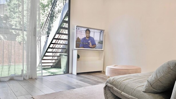 Een moderne woonkamer met een bank, een televisie, een trap en uitzicht op het groen.