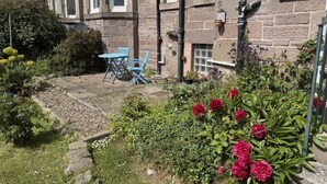 A stone building with a garden, a blue chair, and a flower bed. - Stylish River View Stay Sleeps 6 (Dundee)