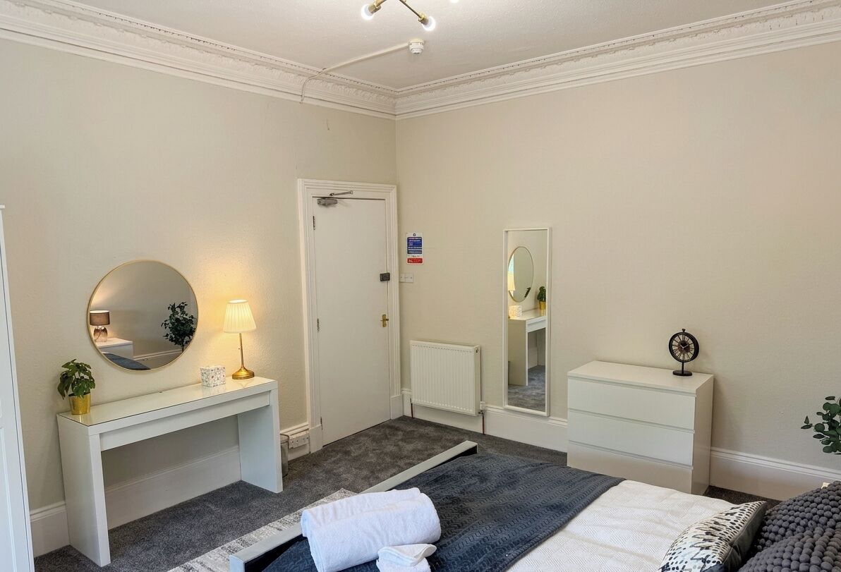 Une chambre à coucher avec un lit, une table de chevet, une lampe, un miroir et une porte.