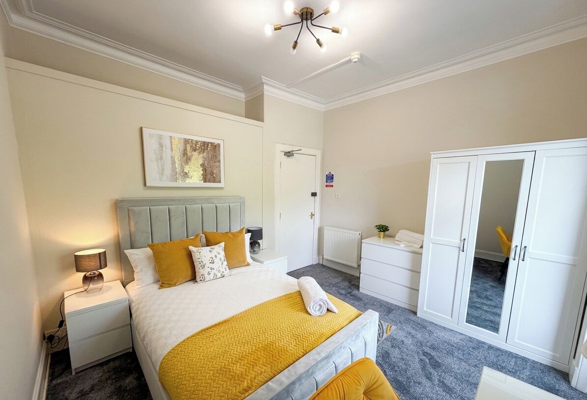 A bedroom with a bed, bedside table, nightstand, wardrobe, and a ceiling light fixture.