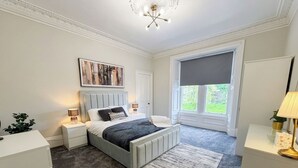 A bedroom with a bed, bedside tables, a nightstand, a window, and a ceiling light fixture. - Stylish River View Stay Sleeps 6 (Dundee)