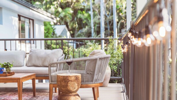 A deck with a sofa, a chair, a wooden table, and a railing.