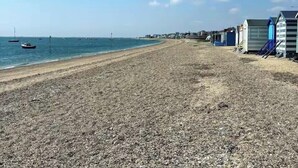 A beach with pebbles, a clear sky, and a row of blue beach huts.