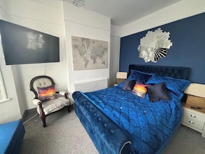 A bedroom with a large bed, a chair, a world map, and a decorative wall piece. - Coastal House opposite beach sleeps 6 Pet friendly (Southend-on-Sea)