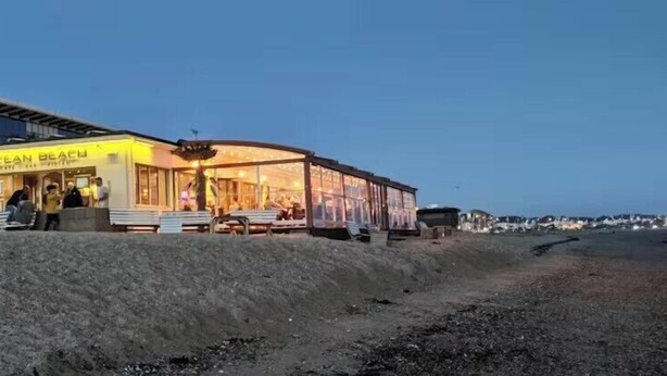 A building with a sign reading 'OCEAN BEACH' and a covered outdoor seating area.