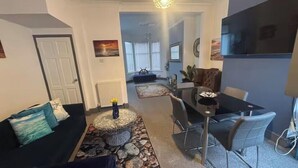 A living room with a sofa, a dining table with chairs, a TV, and a fireplace.