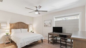 Ein Schlafzimmer mit Bett, Schreibtisch, Stuhl, Deckenventilator und einem Fenster mit Jalousien.