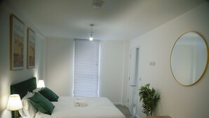 Ein Schlafzimmer mit Bett, Nachttischlampe, Spiegel und einer Tür zu einem anderen Raum.