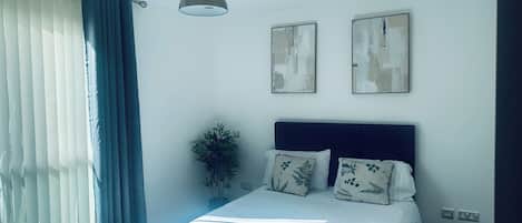 A bedroom with a bed, a ceiling fan, a window with curtains, and two wall-mounted artworks.