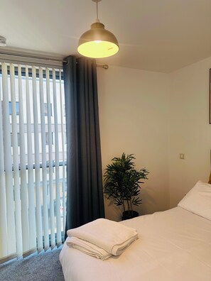 Een hotelkamer met een bed, een potplant en een raam met jaloezieën.