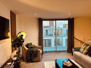 Ein modernes Wohnzimmer mit Sofa, Couchtisch, Fernseher und einem Balkon mit Blick auf Gebäude.