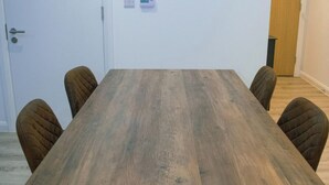 Ein rechteckiger Holztisch mit vier gepolsterten Stühlen, eine weiße Tür und ein Thermostat an der Wand.