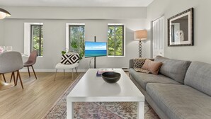 Een moderne woonkamer met een flatscreen televisie, een grijze bank, een witte salontafel en een vloerkleed met een patroon.