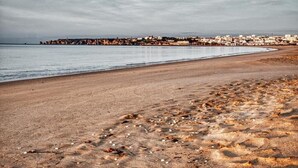 En strand med sandet bredde, et roligt hav og en by i det fjerne.