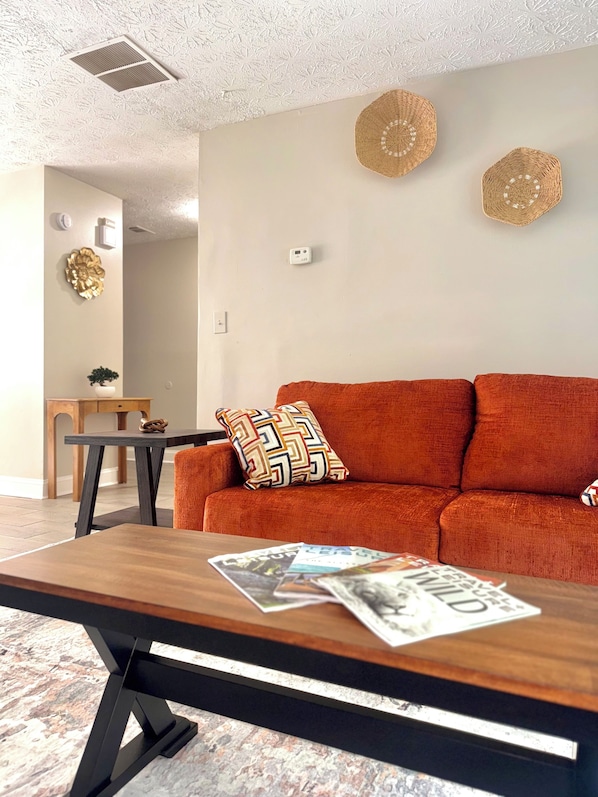 Un salon comprenant un canapé, une table basse avec des magazines, une petite table avec une plante et un mur décoré de différents objets.