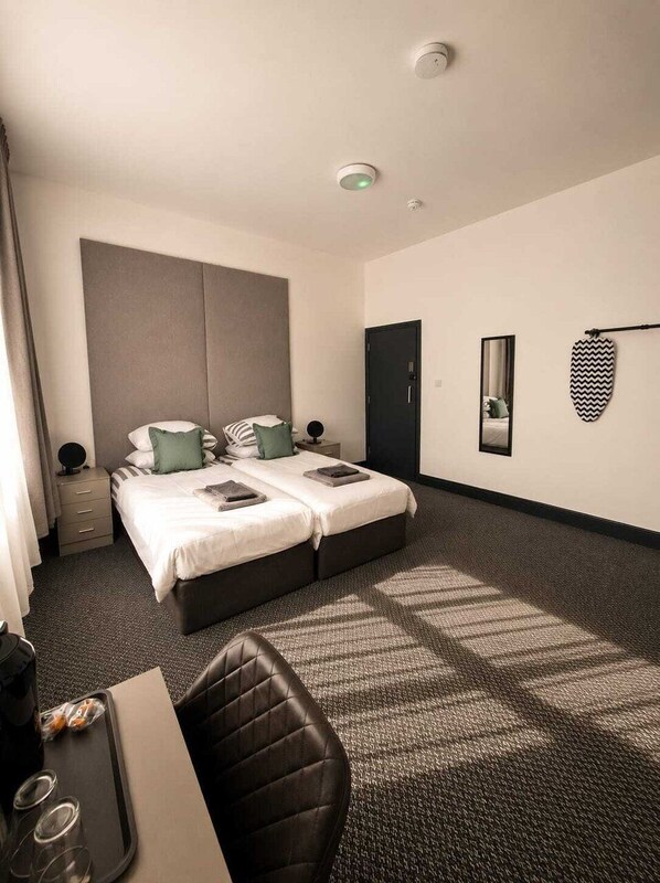 A hotel room with a double bed, a desk, a chair, a small table with a tray, and a mirror on the wall. - Stylish Double Room in Convenient Location (Liverpool)