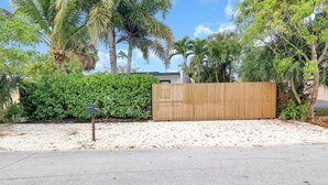 A gated area with a wooden fence, a concrete path, and various tropical plants.