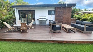 A modern outdoor deck with a grill, seating, and a glass door leading to a patio.
