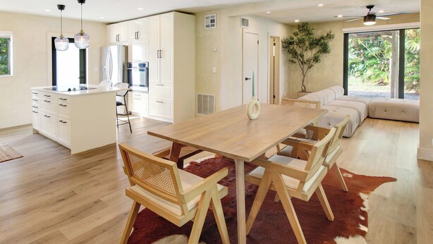 A modern kitchen with white cabinetry, a wooden dining table, and a large window.