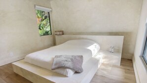 A minimalist bedroom with a bed, a small window, and a nightstand.