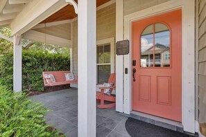 A covered porch with a red door, a bench, and a chair.