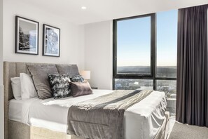 Une chambre d’hôtel moderne avec un grand lit, une vue sur la ville et deux tableaux encadrés au mur.
