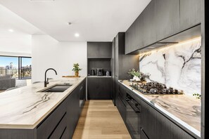 Une cuisine moderne dotée d’un plan de travail en marbre, de meubles de rangement aux couleurs sombres et offrant une vue sur la ville.