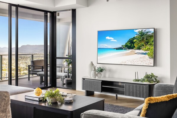 Ein modernes Wohnzimmer mit großem Fernseher, einer Couch, einem Couchtisch mit Dekoration und einem Balkon mit Blick auf die Stadt.