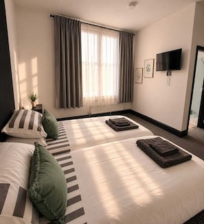 A hotel room with two beds, a TV, a window with curtains, and a plant.