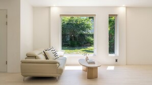 Una sala de estar moderna con un sofá, una mesa de centro y dos ventanas con vistas a un jardín.