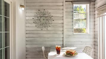 A dining area with a white table, chairs, a decorative wall piece, and a window with a view of trees.