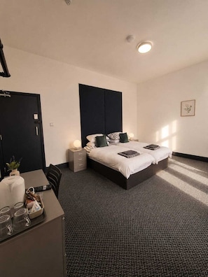 Una habitación de hotel moderna con una cama grande, mesitas de noche, un escritorio con una silla y una pequeña planta.
