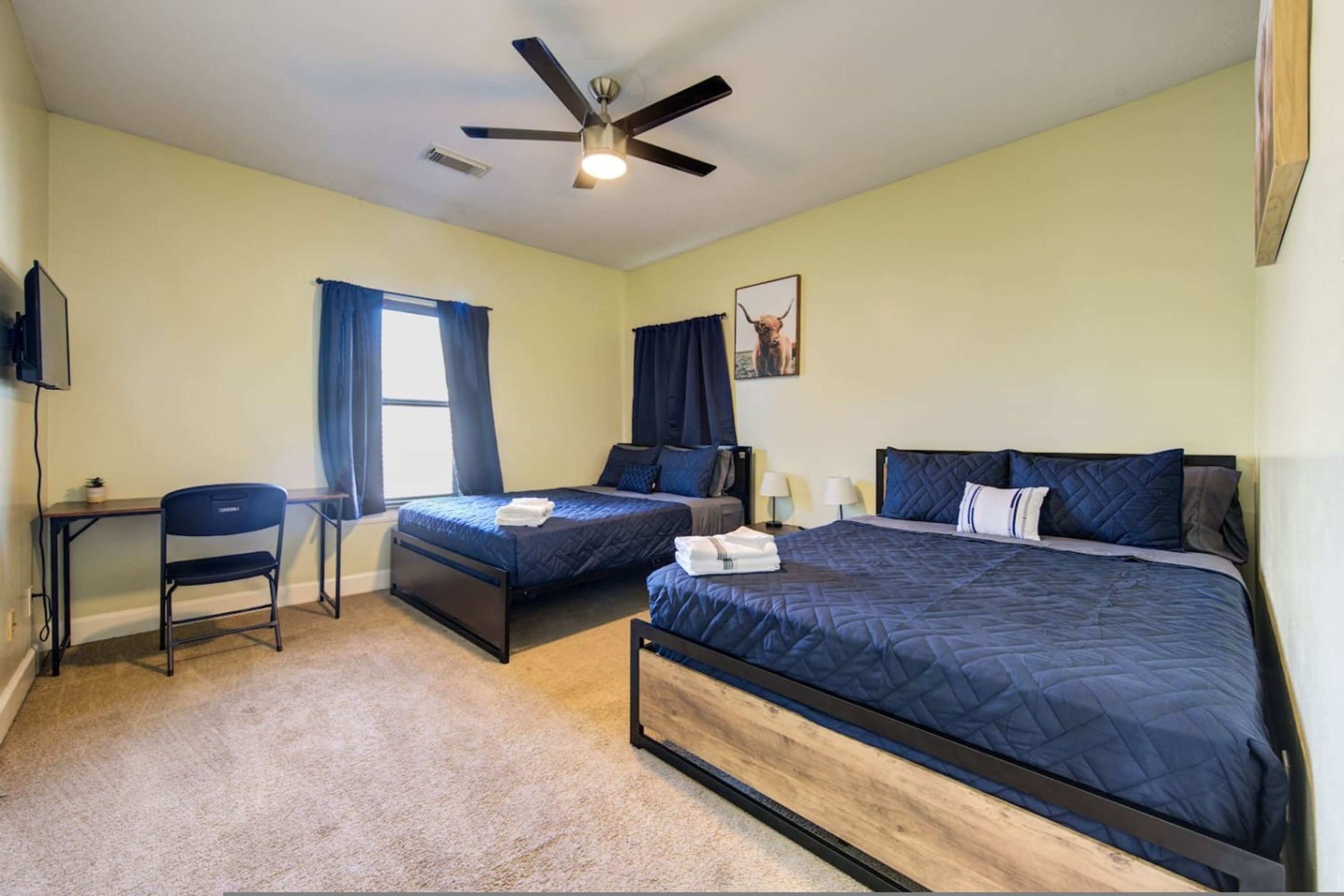 A bedroom with two single beds, a desk, a chair, a ceiling fan, and a TV.