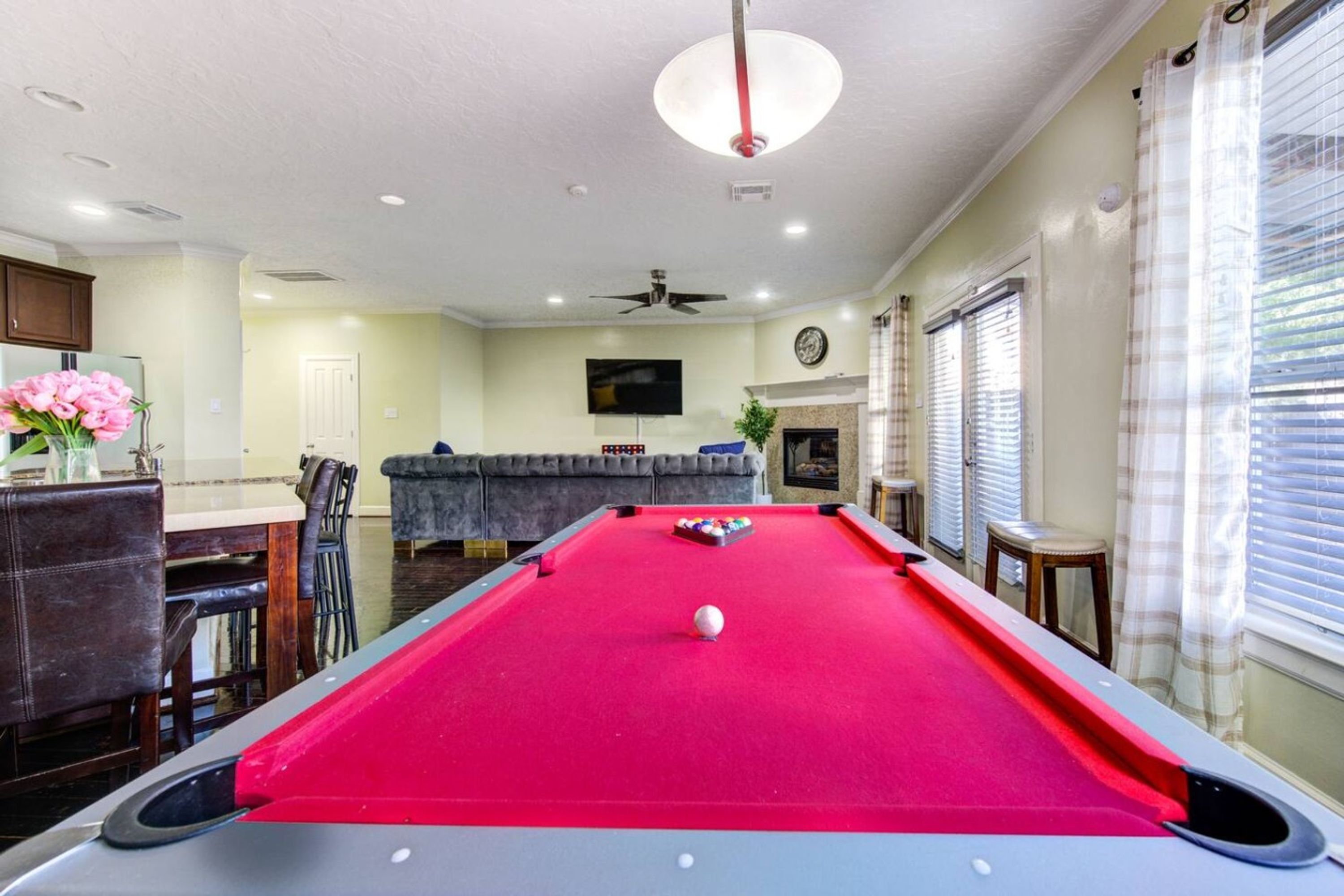 A pool table in a room with a ceiling fan, a television, and a dining area with chairs and a table.