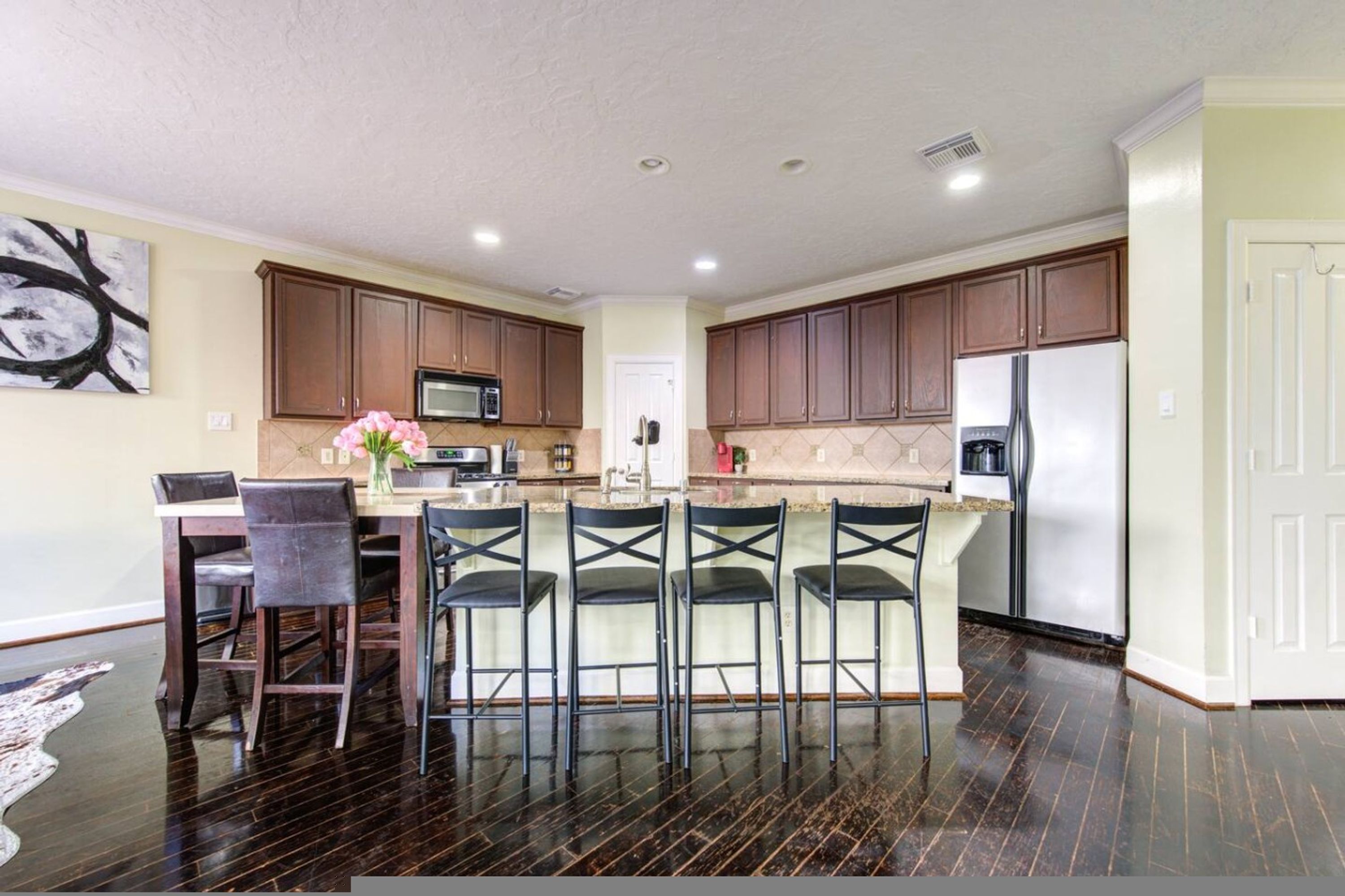A modern kitchen with dark wood cabinets, a central island with bar stools, a microwave, and a refrigerator.