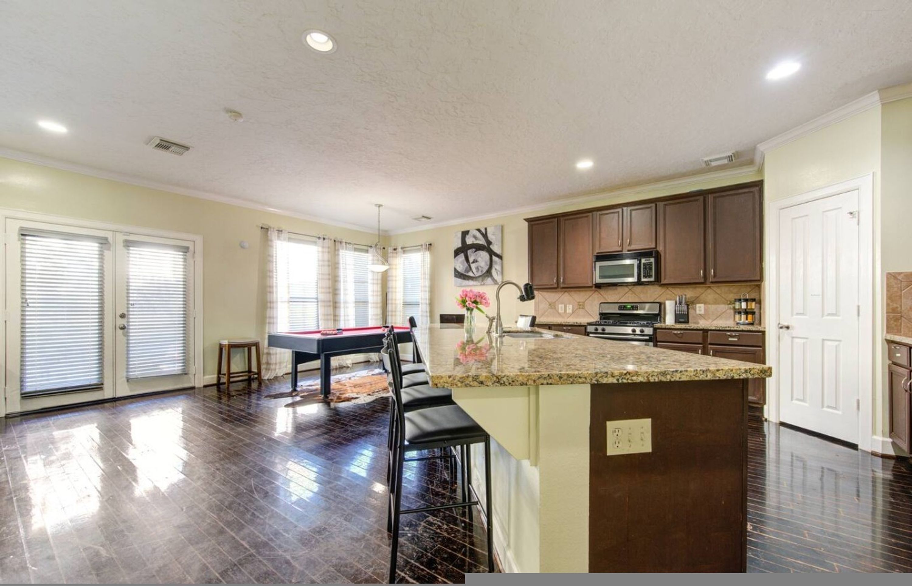 A spacious kitchen with dark flooring, a dining area, and a bar with stools.