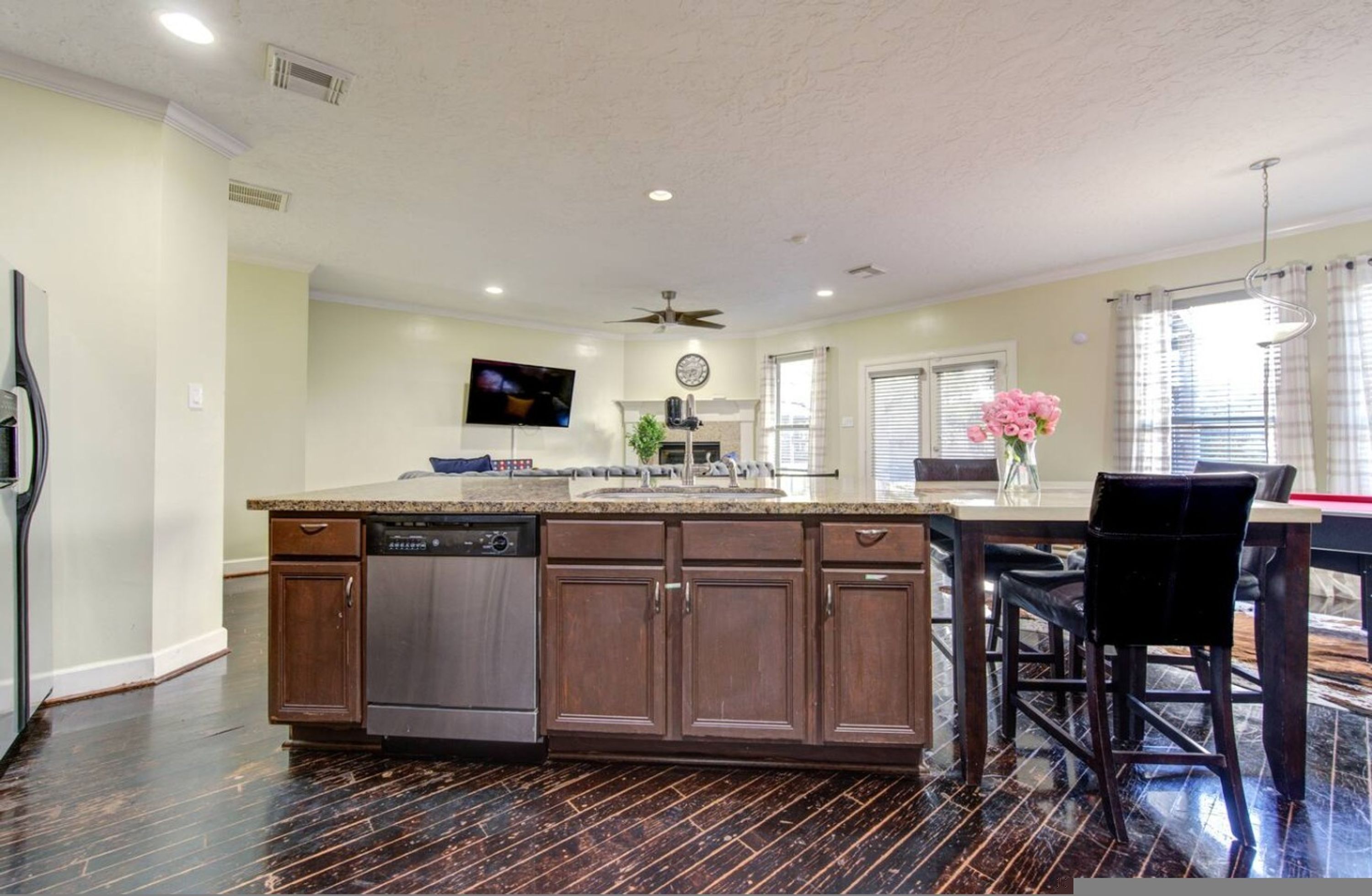 A kitchen with dark wood cabinets, a dishwasher, a large island with a sink, a ceiling fan, and a TV mounted on the wall.