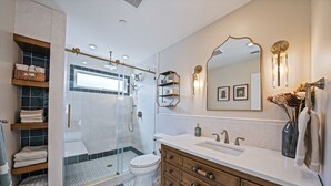 Un baño moderno con ducha envuelta en vidrio, inodoro blanco, tocador de madera con lavabo y un espejo grande.