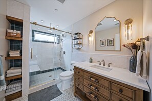A modern bathroom with a glass-enclosed shower, a white toilet, a wooden vanity with a sink, and a large mirror. - 4 Bedroom House Minutes from the beach! (Long Beach)