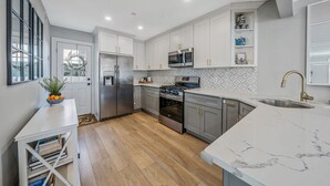Una cocina moderna con armarios blancos, electrodomésticos de acero inoxidable, encimera de mármol y horno empotrado.