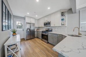 A modern kitchen with white cabinetry, stainless steel appliances, a marble countertop, and a built-in oven. - 4 Bedroom House Minutes from the beach! (Long Beach)